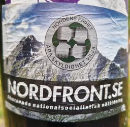 Sticker featuring a logo with four clenched fists in a circle, mountains in the background, and the text "Nordens Frihet " ("Freedom of the North") and "Ara Skyndighet Vilja" ("Race, Honor, Will") around the fists.  The bottom of the sticker displays the website address nordfront.se and describes it as an independent National Socialist online newspaper.