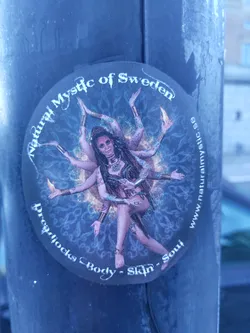 Round sticker featuring an illustration of a woman with multiple arms, reminiscent of a Hindu goddess, in a cosmic mandala. Text on the sticker includes the brand name, location, and a tagline emphasizing dreadlocks, body, skin, and soul.