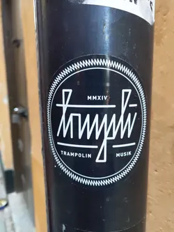 Black and white round sticker with the text "Trampolin Musik" and the year MMXIV (2014) in the center. The design is minimalist with a unique typography style.