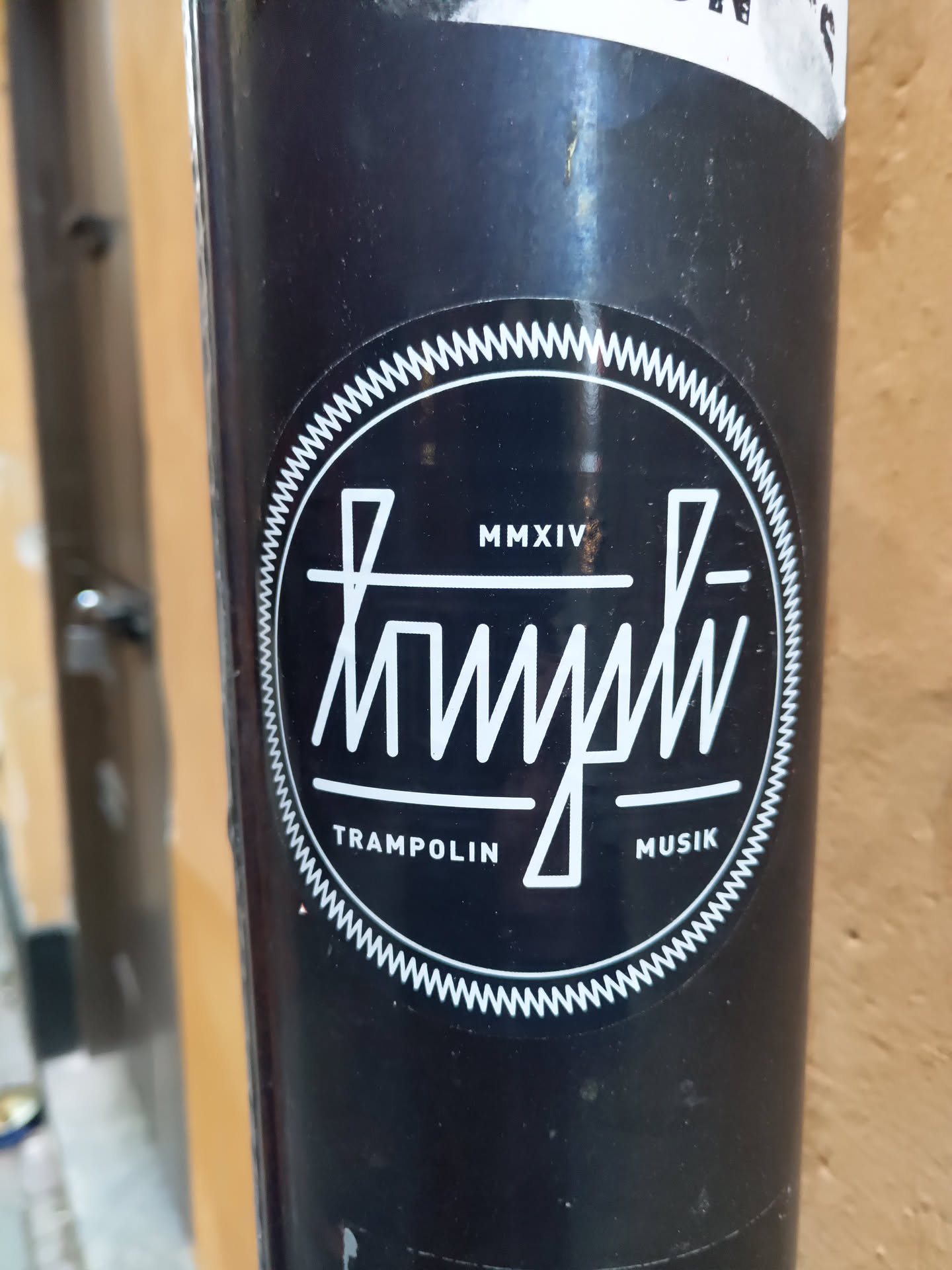 Black and white round sticker with the text "Trampolin Musik" and the year MMXIV (2014) in the center. The design is minimalist with a unique typography style.