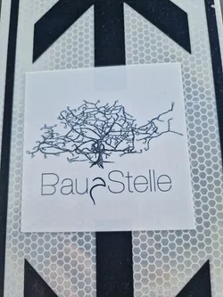 A minimalist sticker featuring a stylized tree illustration and the word "BauStelle" (German for construction site) underneath.  The design is printed on a white background. 