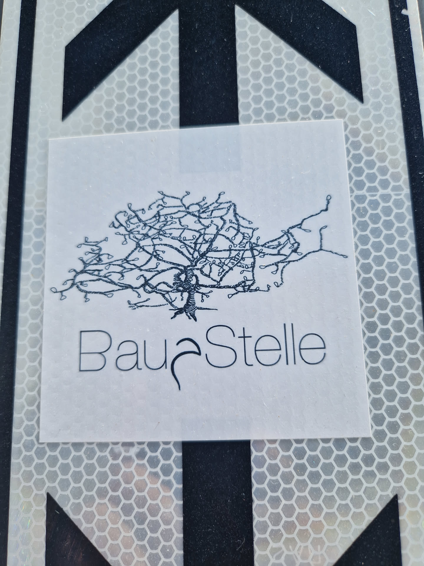 A minimalist sticker featuring a stylized tree illustration and the word "BauStelle" (German for construction site) underneath.  The design is printed on a white background. 