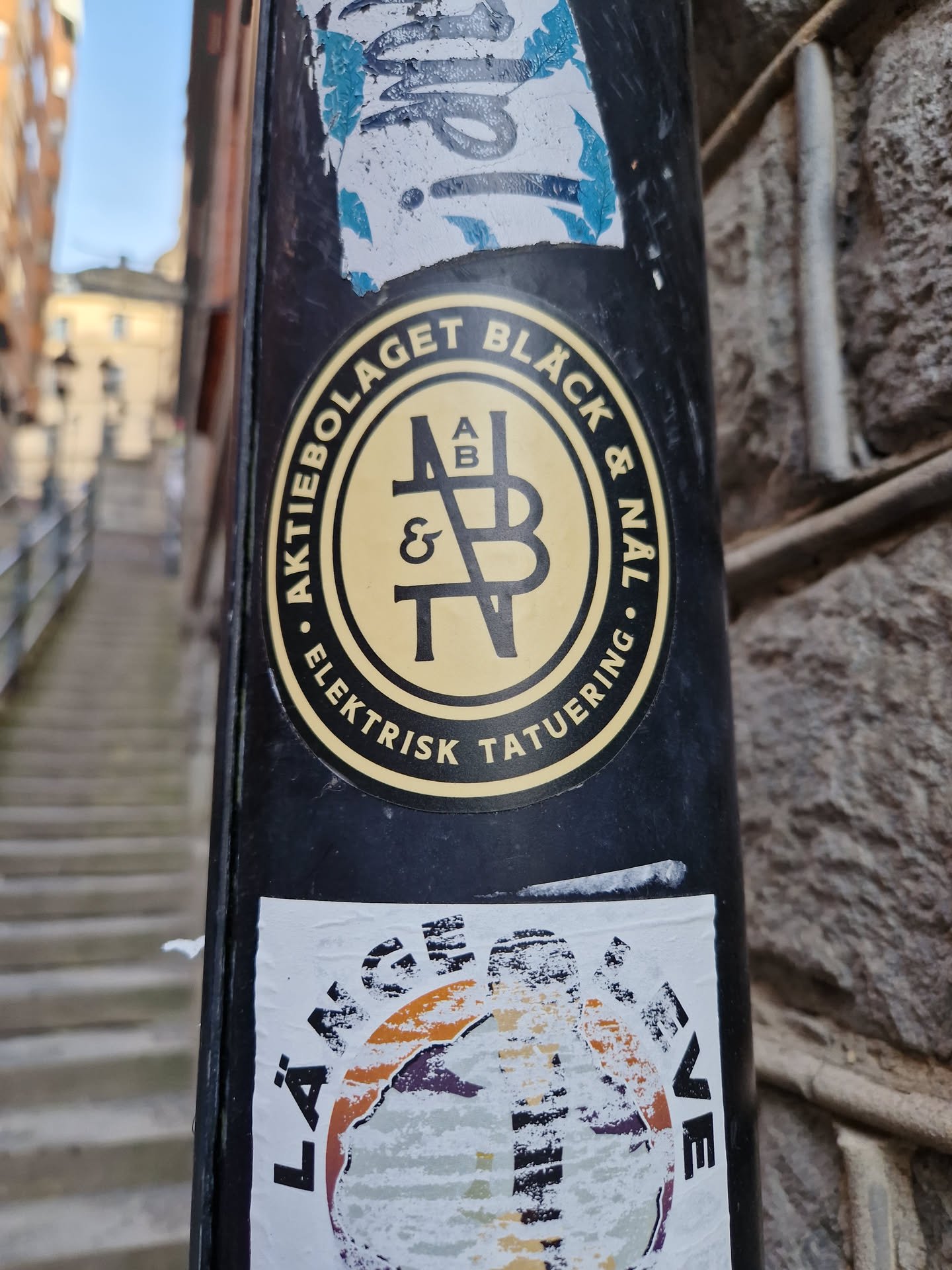 A sticker featuring a logo for Aktiebolaget Black & Navy, which seems to be an electric tattooing company. The logo is a circular design with the company name written around it and stylized initials in the center. The sticker is black and yellow. 
