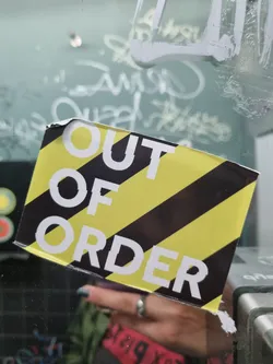 A sticker with black and yellow stripes and the text "OUT OF ORDER" in white. The sticker is stuck on a glass surface.