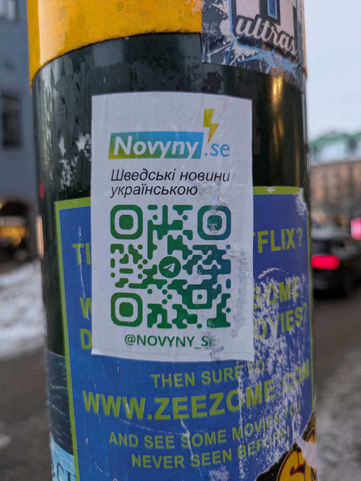 This sticker advertises Nowyny.se, a news source for Ukrainian news in Sweden.  It includes a QR code linking to their online presence and their Instagram account. The text on the sticker is in Ukrainian and Swedish.