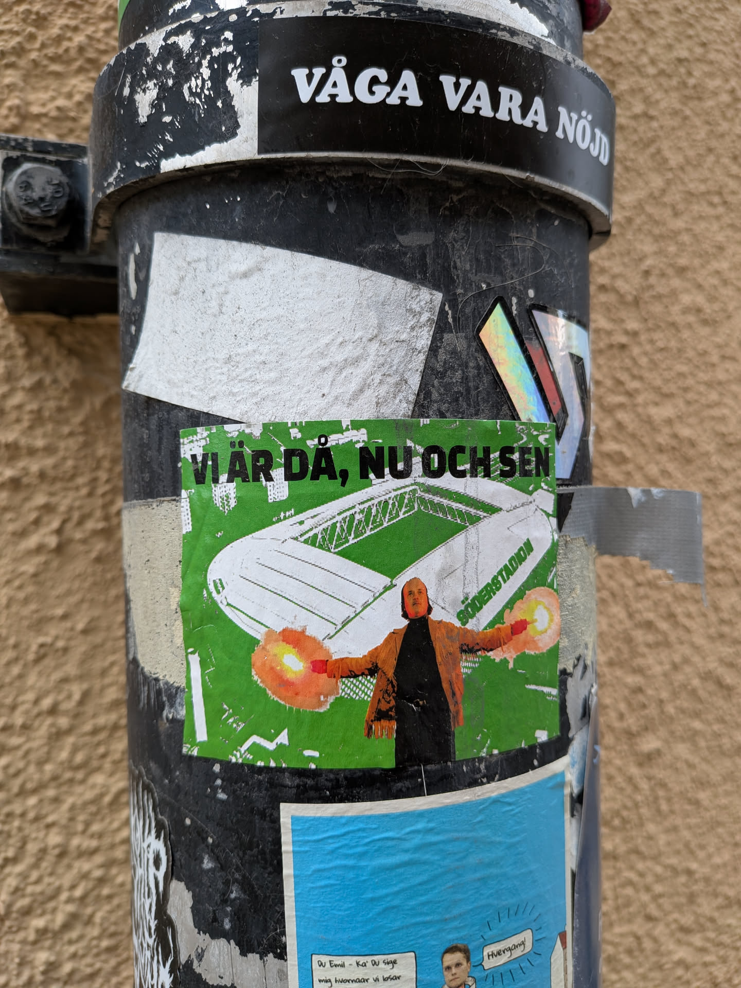 A rectangular sticker featuring a vibrant green background. At the top, bold black text reads 'VI ÄR DÅ, NU OCH SEN'. Below this, a white outline drawing depicts a stadium, identified by the text 'SÖDERSTADION' along its side. In the foreground, a person with an orange-brown jacket and dark clothing stands with arms outstretched, holding two brightly lit orange and yellow flares. The overall aesthetic evokes football fan culture and loyalty.