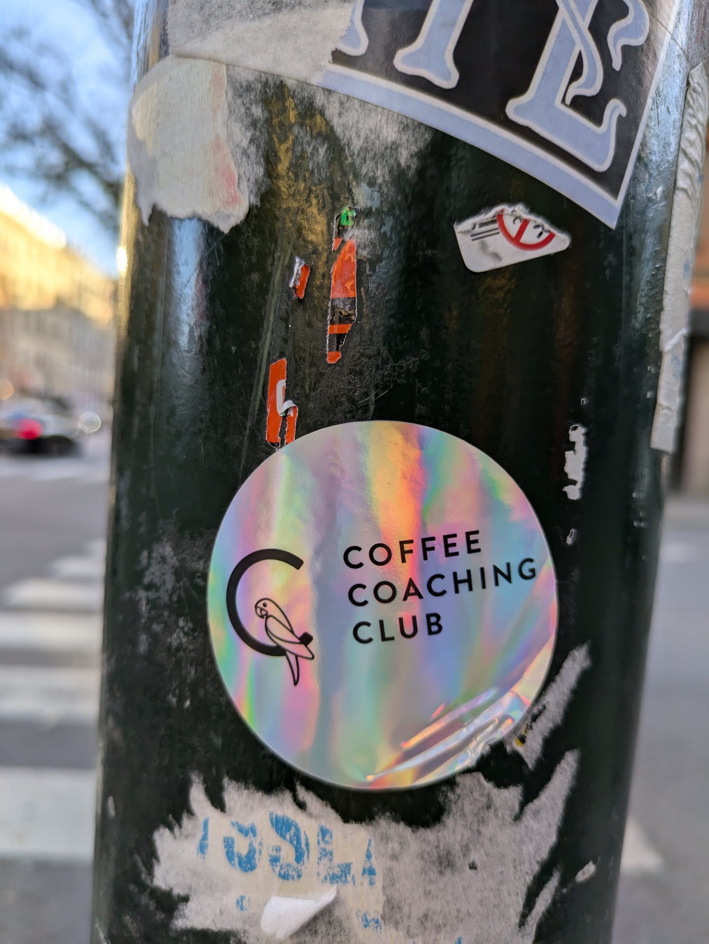 A holographic sticker for the Coffee Coaching Club.  The sticker features a minimalist design with a bird illustration and the club's name. 