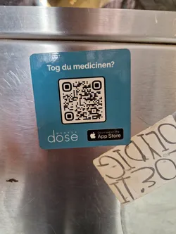 A teal colored sticker with a QR code and the text "Tog du medicinen?" which translates to "Take your medication?" in Danish.  It also features the Medbox Dose logo and links to download the app from the App Store. 