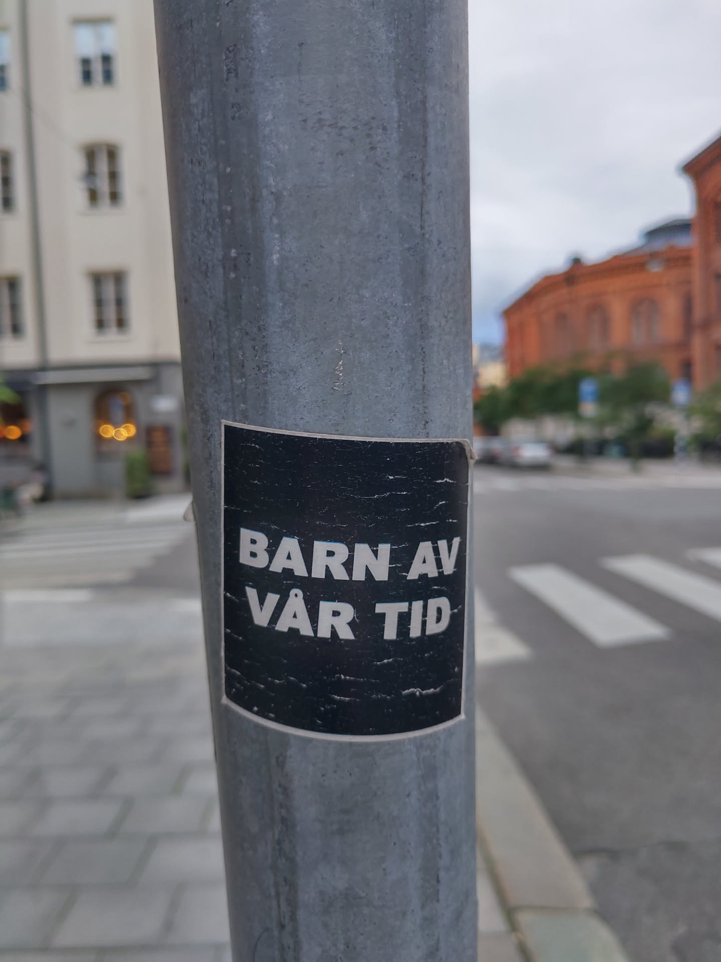 A black and white sticker on a metal pole. The text on the sticker says "Barn av vår tid" which translates to "Children of our time" in Swedish.