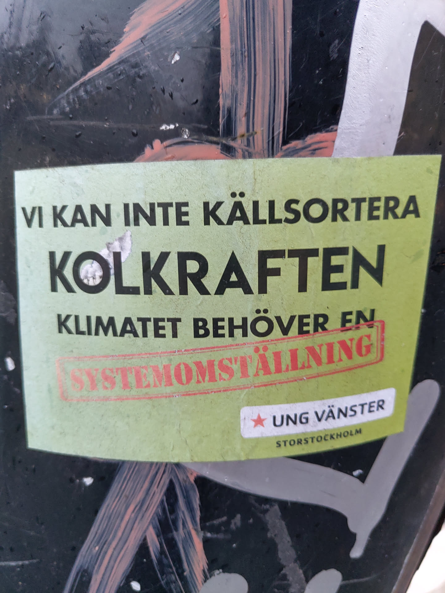 A green sticker with text in Swedish that translates to: We cannot recycle coal power. The climate needs a system change.  The sticker features the logo of Ung Vänster (Young Left) Storstockholm.