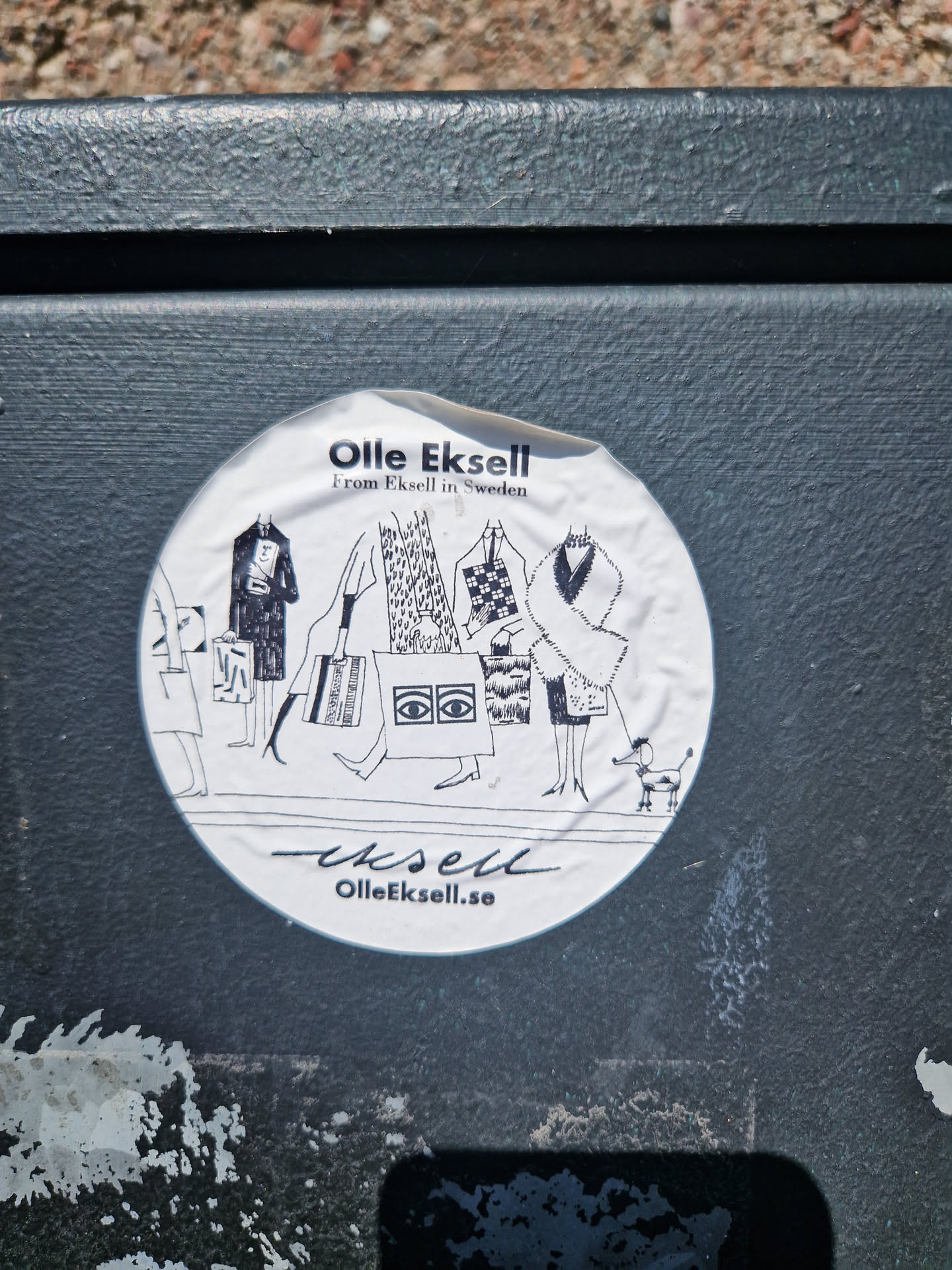 Round sticker featuring a black and white illustration of people shopping and a dog. The text includes the artist's name, origin and website.