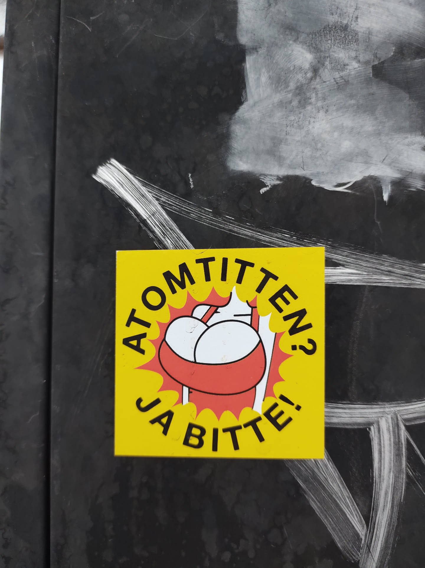 Yellow sticker with a cartoon illustration of a person carrying two large breasts in a red basket. The text on the sticker says "Atomtitten? Ja bitte!" which translates from German to "Atomic boobs? Yes please!"