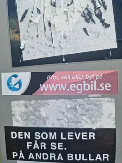 A sticker with a quote in Swedish. It says: "He who lives will see. On other buns." It's placed on top of another sticker which advertises a website.
