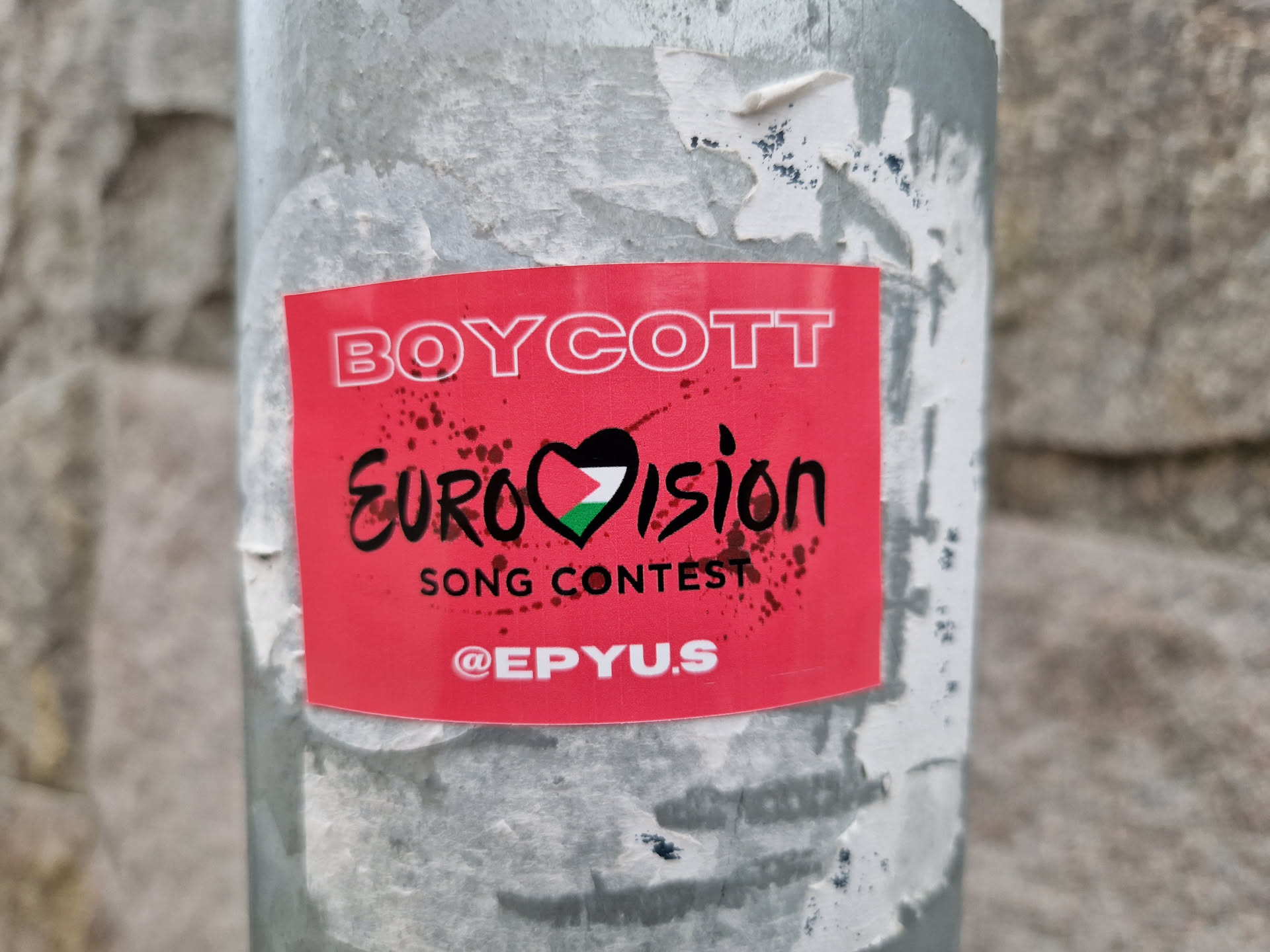 A red sticker with white and gray text expressing a boycott of the Eurovision Song Contest.  The sticker includes a heart incorporating the Palestinian flag. 