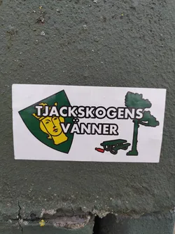 A sticker featuring a crest with a crowned woman's face, a pine tree, and a picnic table. The text on the sticker says "Tjackskogens Vänner".