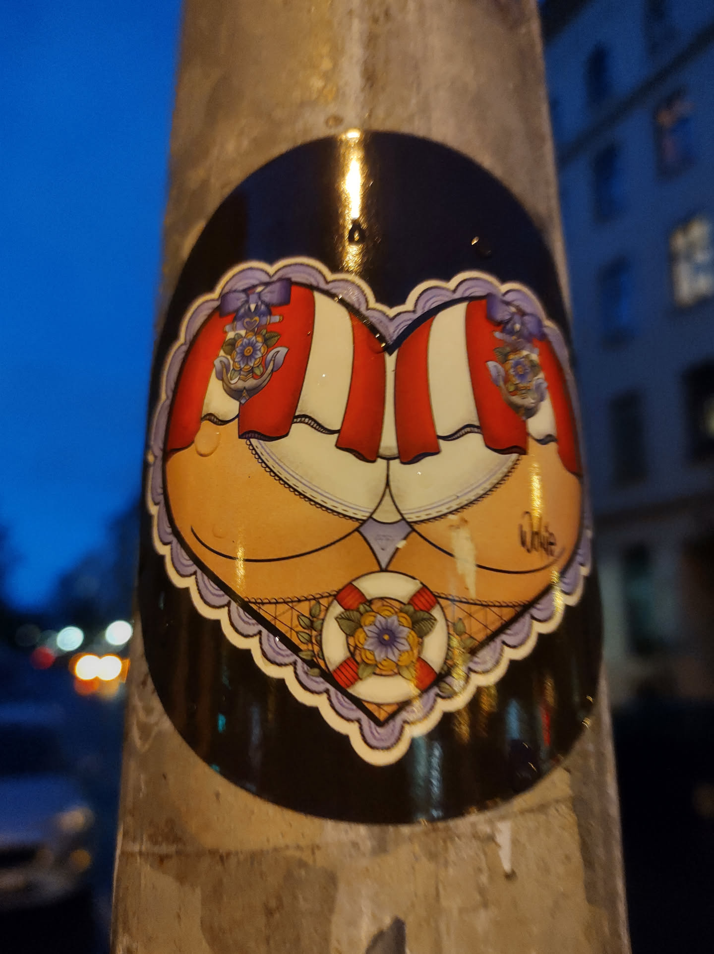 A round sticker with a heart-shaped design shows two backsides, each adorned with a red and white striped canopy.  Nautical elements, including a floral motif and a life preserver, are incorporated into the design. The style is reminiscent of vintage pin-up art or tattoo flash.