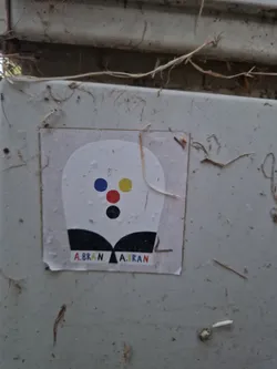 A small, rectangular sticker with a simple design. The main element is a stylized head-like shape with a few colorful dots and a black bottom. The text 'A.BRAN' is repeated twice at the bottom of the sticker.