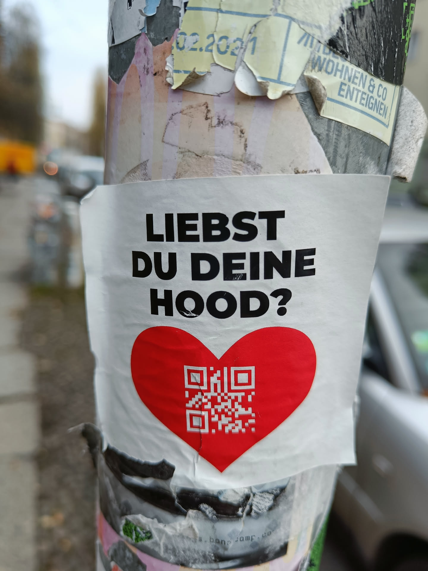 A sticker featuring a red heart with a QR code in the center.  The text on the sticker asks in German, "Do you love your Hood?"