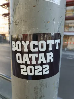 A black and white sticker with the text "BOYCOTT QATAR 2022" pasted on a pole.