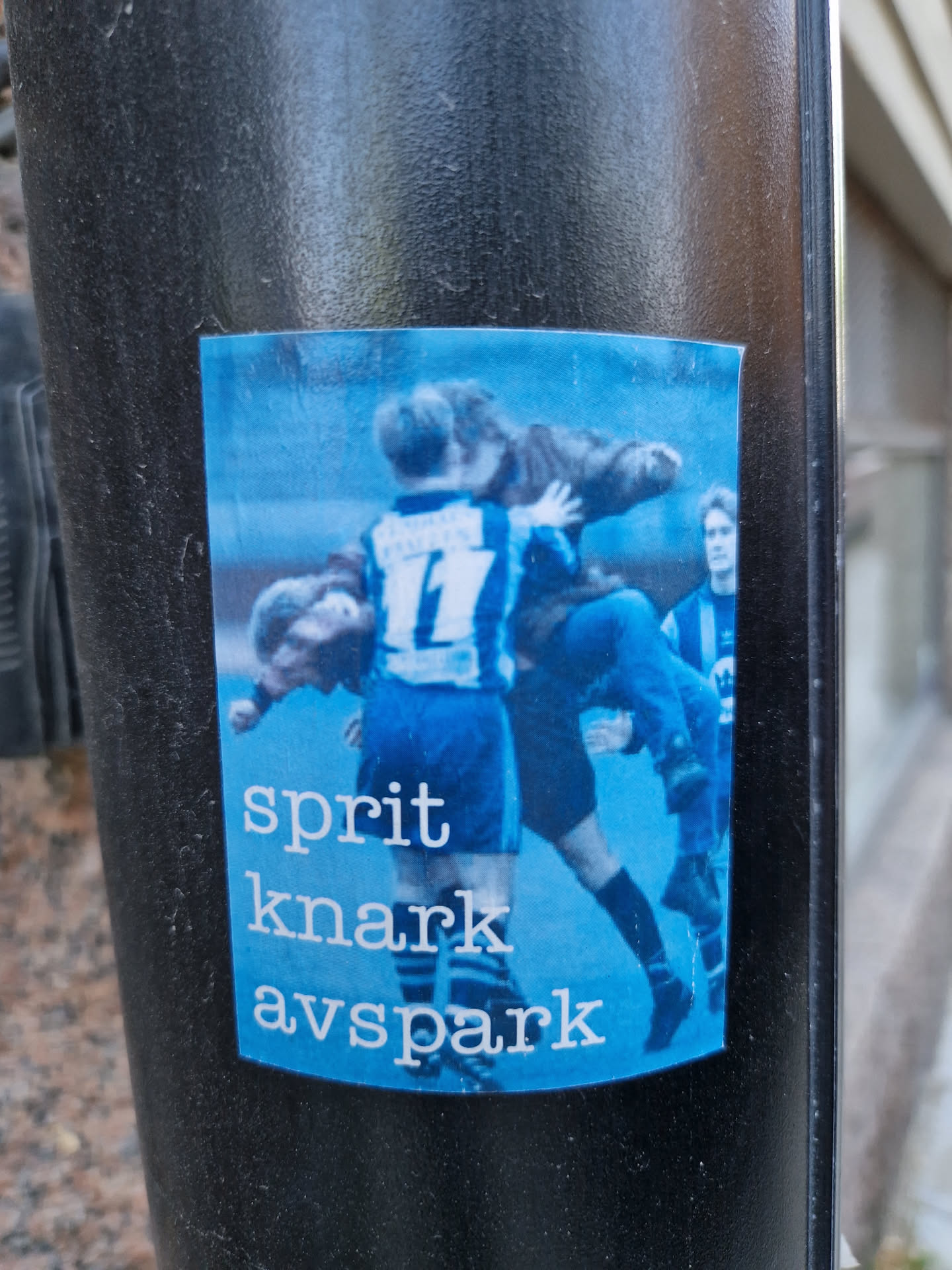 The sticker shows a dynamic scene from a football game, possibly a tackle or a moment of intense action. Three players are clearly visible, two in dark blue shirts, and one in a lighter color. The background is a blurry, action-filled football field.  Below the image, three words are written: "sprit", "knark", and "avspark."  These words are written in a simple, sans-serif font.