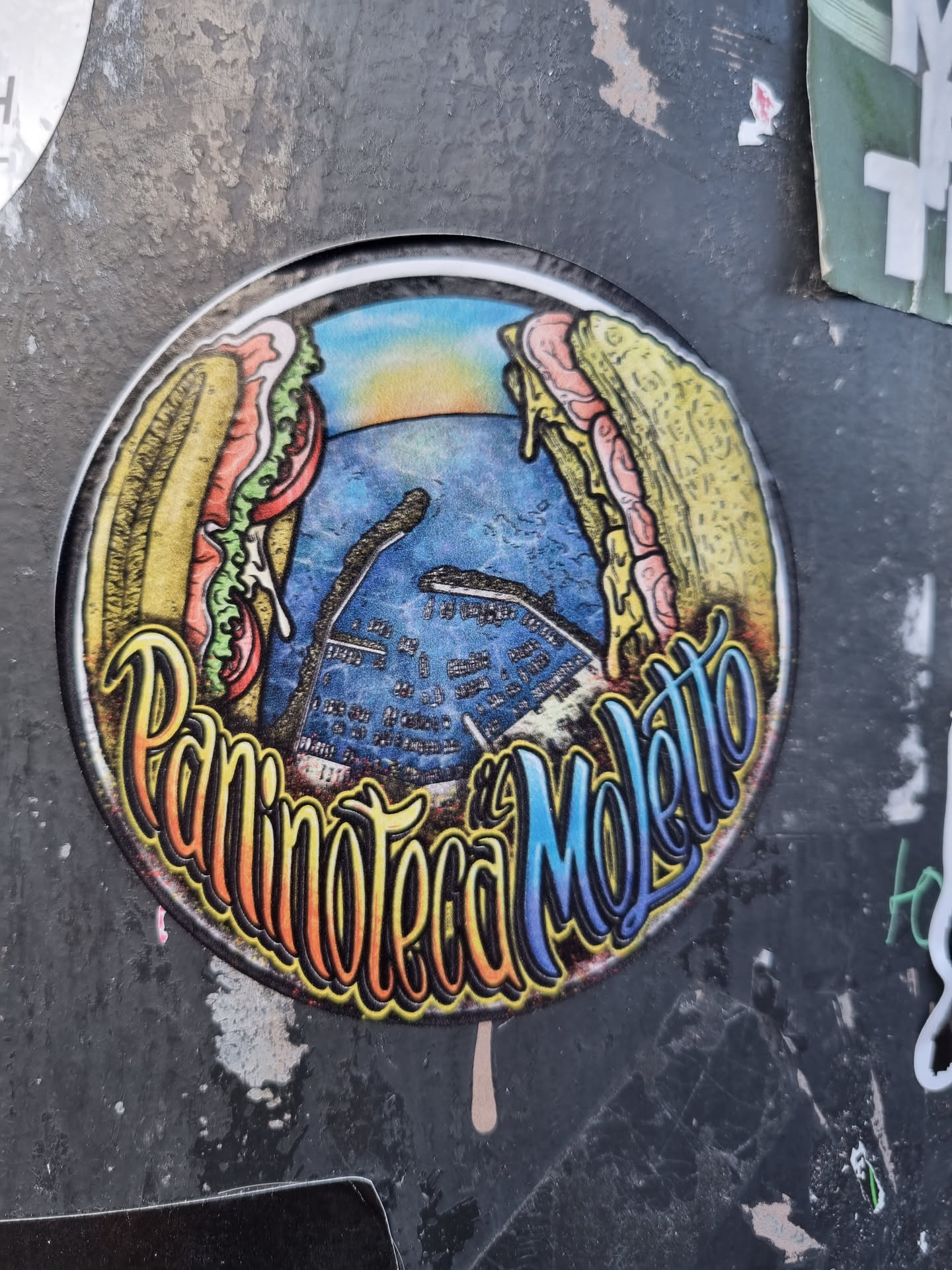 A round sticker featuring an illustration of two large sandwiches flanking a stylized seascape. The name "Paninoteca Moletto" is prominently displayed in colorful lettering.