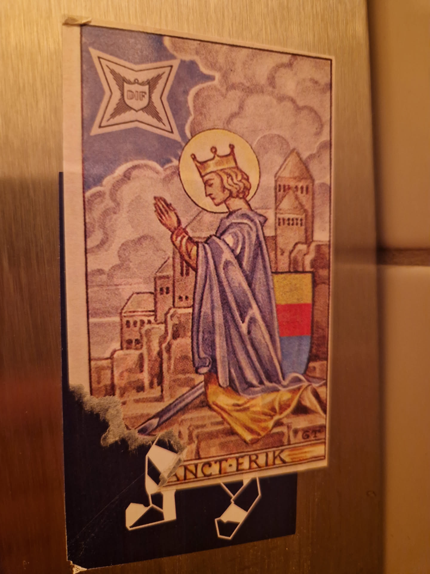 A sticker depicting Saint Eric, King of Sweden, kneeling in prayer before a city.  The artwork is in a style reminiscent of medieval illustrations. The sticker shows some minor damage around the edges.