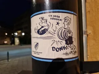 A sticker featuring a cartoon illustration of a comedic scene. One character is hitting another with a ball. There's text on the sticker that says "UR SPÄR BÖNDER!" and "DONK!" which translates from Swedish to English as "You are spoiled farmers!" and "DONK!" respectively. At the bottom of the sticker, there is a logo and text: "STOCKHOLMSLAGET MEDAN 1891".