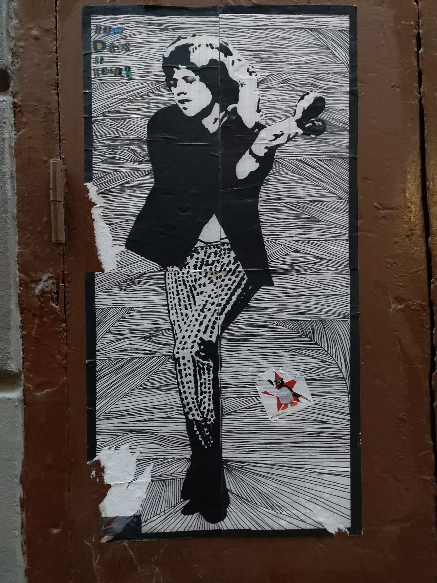 A black and white street art sticker depicting Mick Jagger in a dynamic pose. The art style is reminiscent of a line drawing, with hatched lines creating shading and texture. The sticker is slightly damaged around the edges, suggesting it has been affixed to a surface for some time.  A smaller sticker is visible underneath the main one.