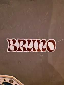 A maroon and white sticker with the name Bruno written in a retro, groovy font. The sticker is applied to a gray surface.