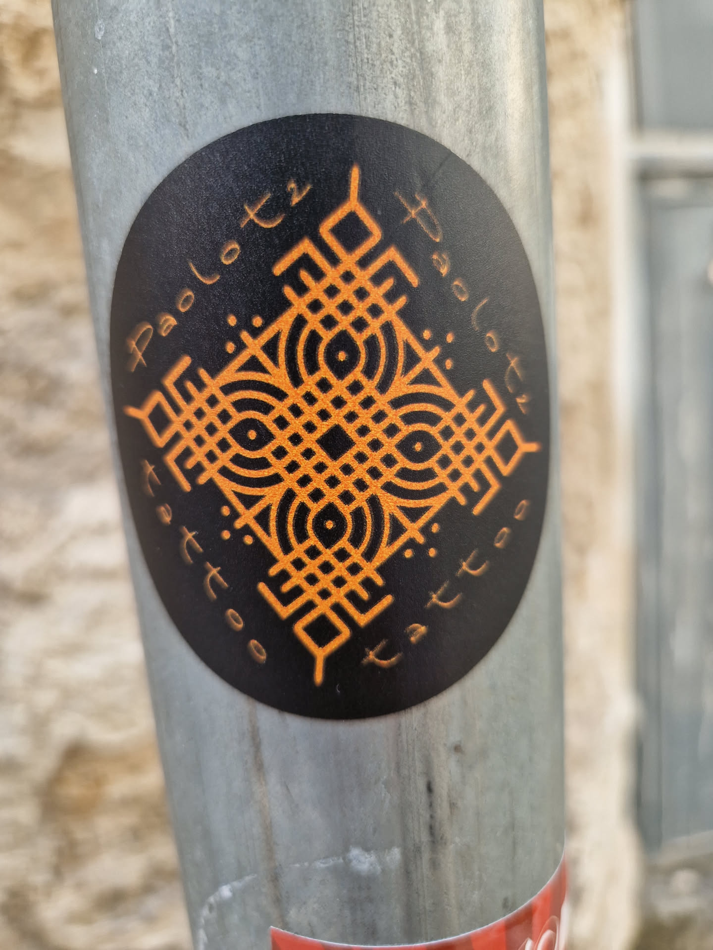 Round black and orange sticker with a geometric design and the text "Paolo Tattoo" written around the edge. The central design features a symmetrical pattern with circles and lines.