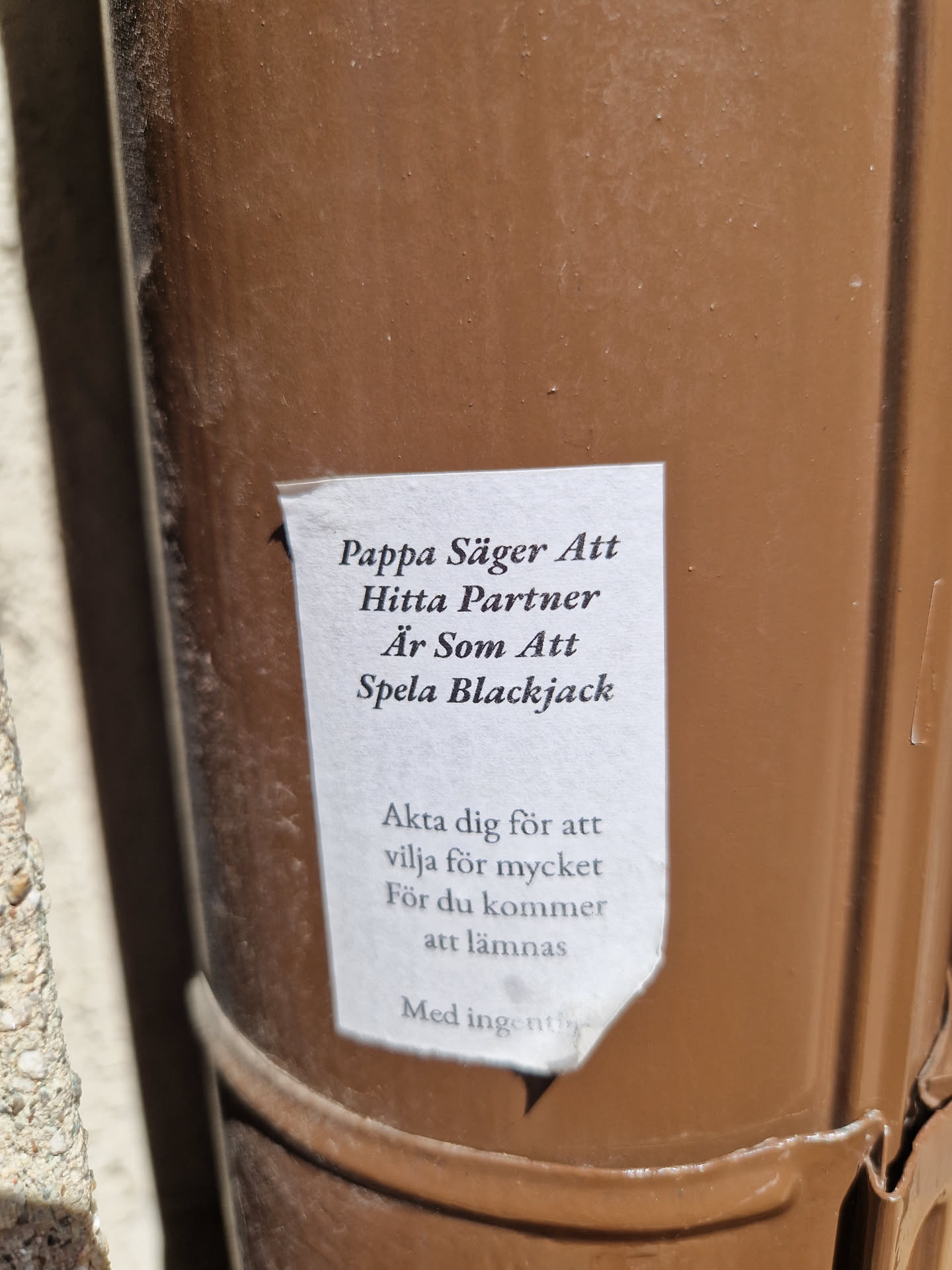 A sticker on a brown pipe with a quote about finding a partner, comparing it to playing blackjack and warning against wanting too much.