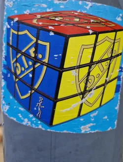 A sticker featuring a Rubik's Cube with shields on each face and a stick figure on one side. The shields have a logo that is partially visible.