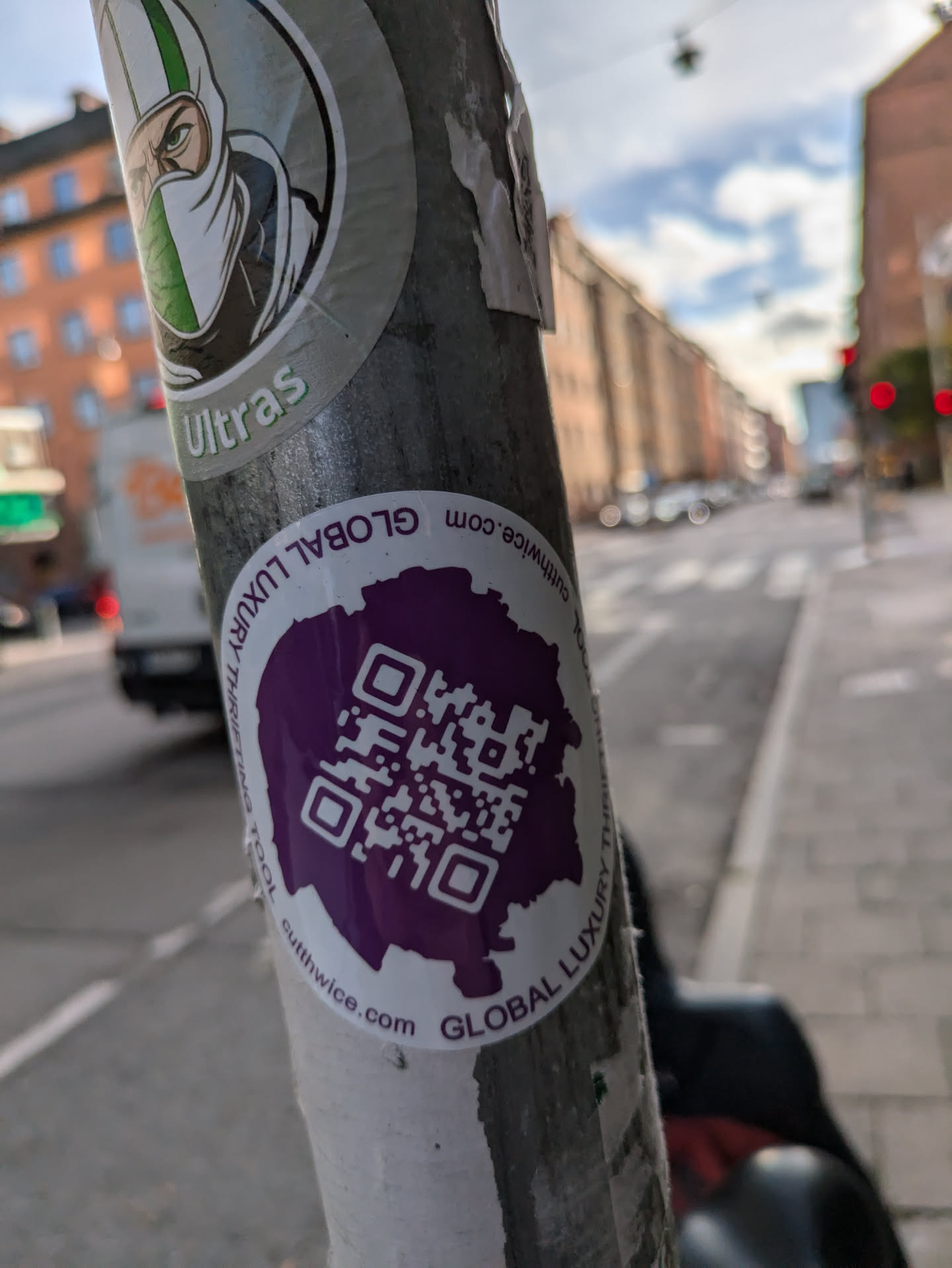 A purple sticker with a QR code in the center. The text "GLOBAL LUXURY TRAVEL" is written around the edge. The background is white. The sticker is attached to a metal pole.