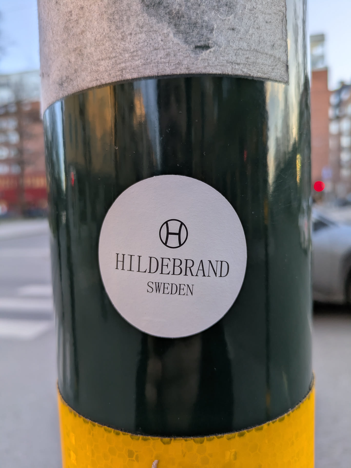 The sticker features the word 'HILDEBRAND' written in bold capital letters, right below a circular logo that's divided in half. Underneath the brand name is the word 'SWEDEN' in smaller letters. It's affixed to a green and yellow pole.