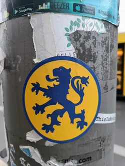 A round sticker on a pole features a blue heraldic lion rampant on a yellow background.  The sticker is slightly worn.