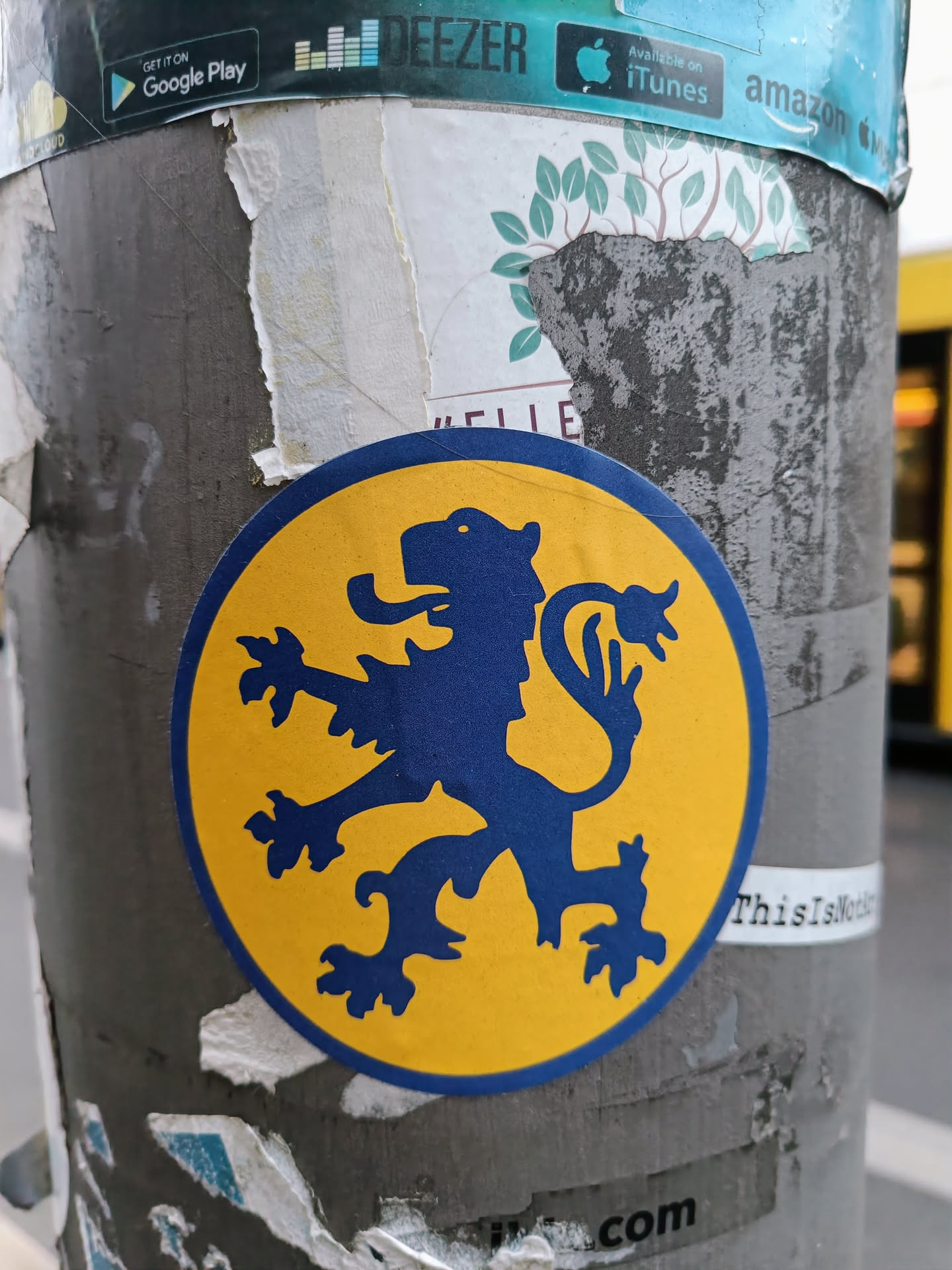 A round sticker on a pole features a blue heraldic lion rampant on a yellow background.  The sticker is slightly worn.