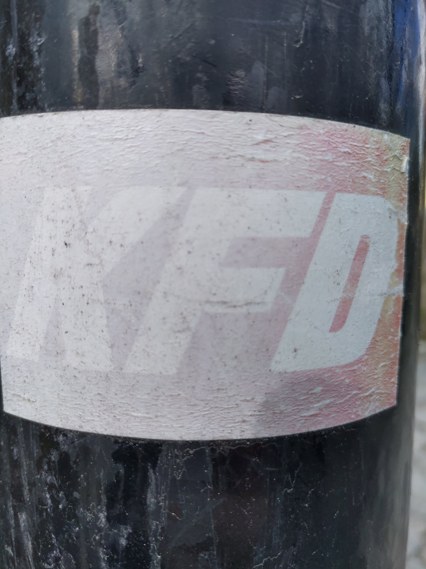 A worn sticker with the letters YFD in a stylized font. The sticker shows signs of wear and tear, suggesting it has been exposed to the elements for some time. The background is primarily white with a subtle gradient, and the lettering is slightly raised from the surface.