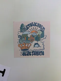 A square sticker featuring a cartoon illustration of Stockholm, Sweden. The illustration includes buildings, mountains, a sun, clouds, and a crown. The text "STOCKHOLM" is at the top and "BLUE TOMATO" at the bottom.
