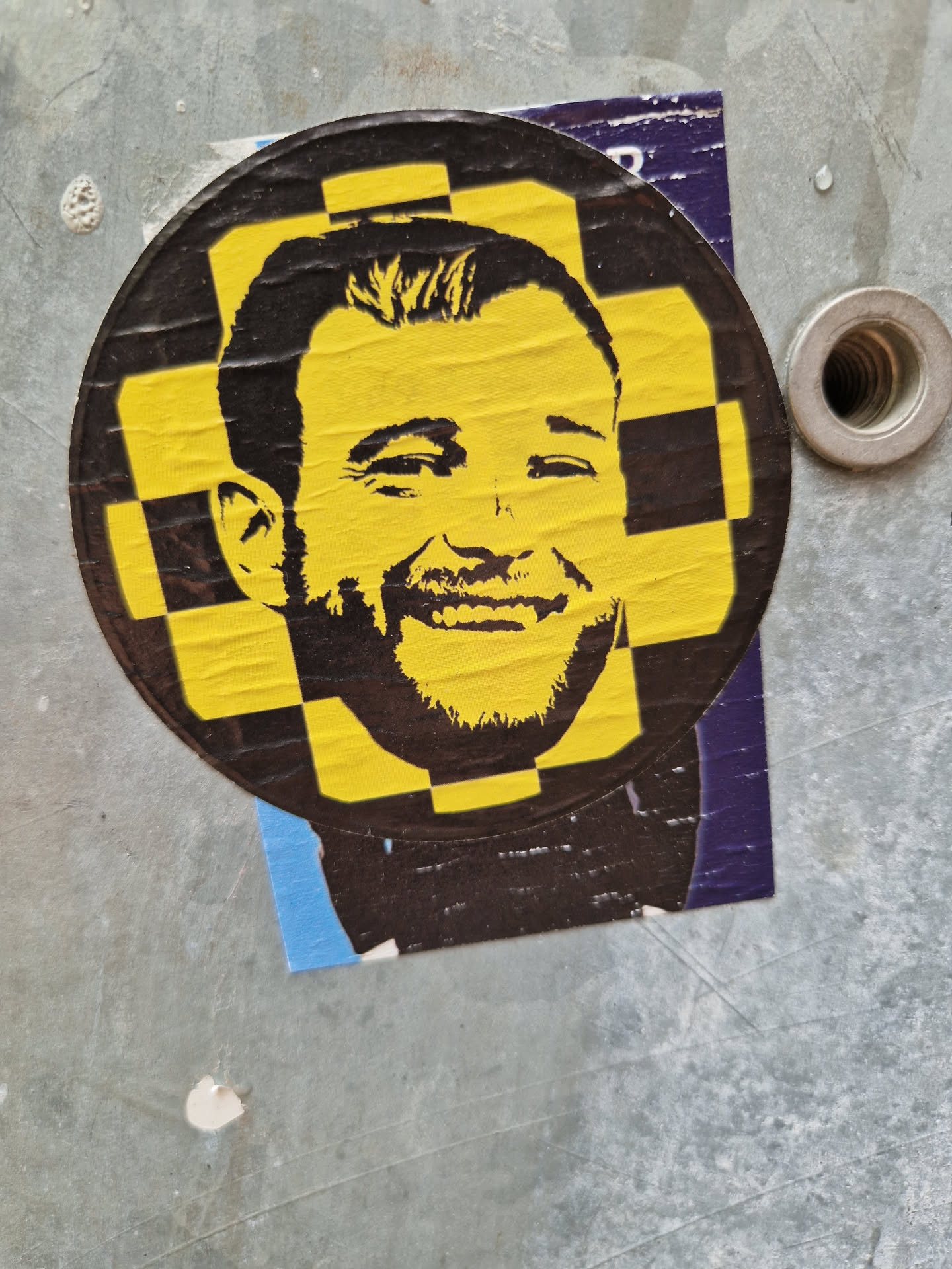 A round sticker featuring a stylized portrait of a man in yellow and black. The style is reminiscent of pop art and stencil art. The image is striking and eye-catching.