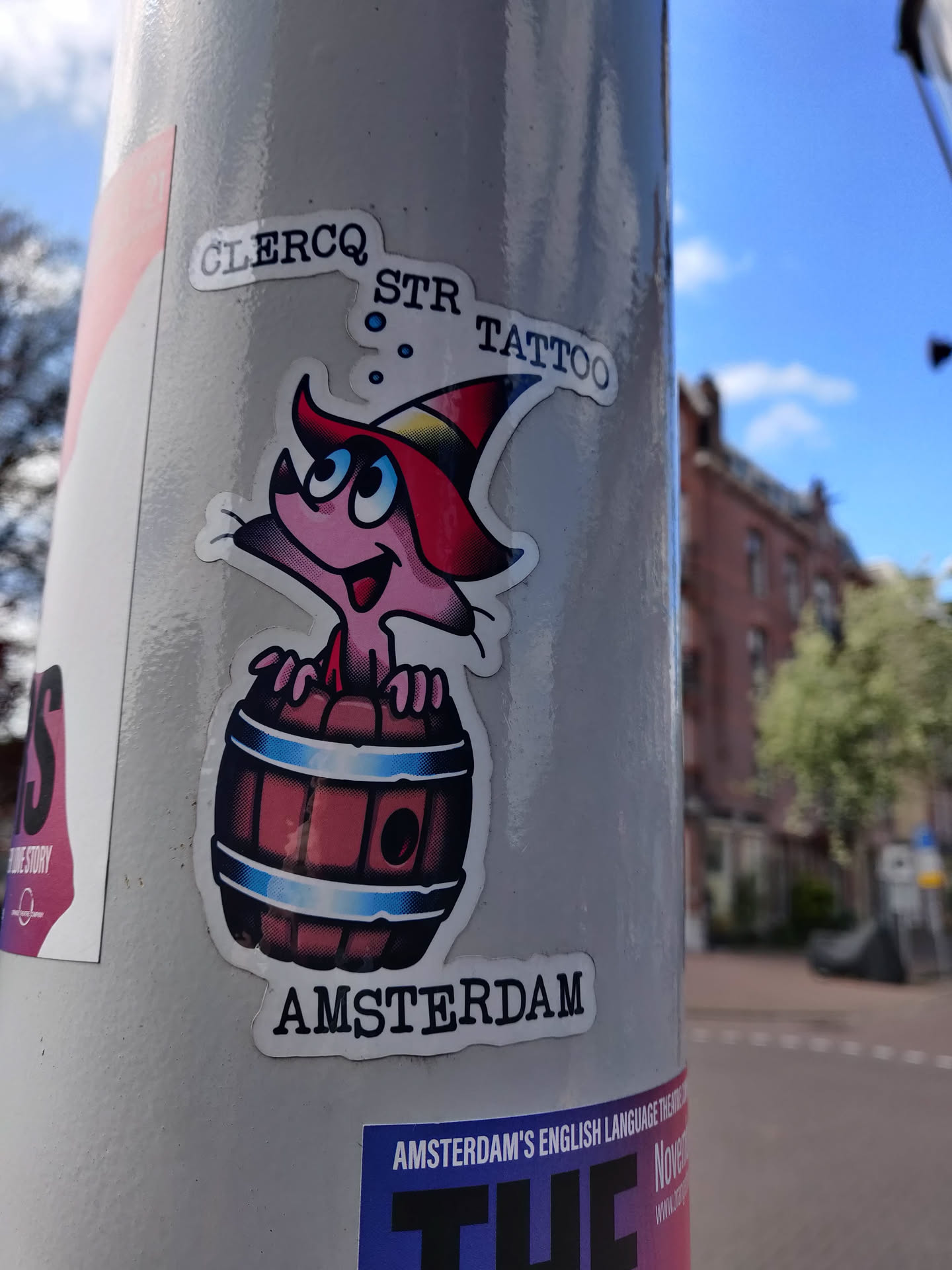 A sticker featuring a cute cartoon character with a wizard hat sitting inside a wooden barrel. The text 'GLERCQ STR TATTOO' and 'AMSTERDAM' are visible on the sticker.