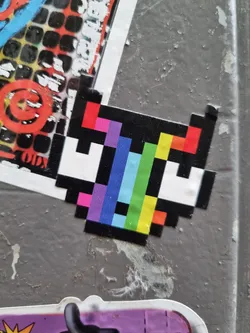 A pixel art sticker featuring a creature with rainbow colored pixels. The sticker has a retro video game aesthetic.