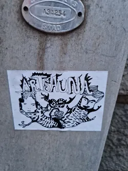 A black and white sticker with the word ARTSAUNA in a stylized font. The design includes abstract figures that resemble animals or mythical creatures. The style is reminiscent of psychedelic or folk art.