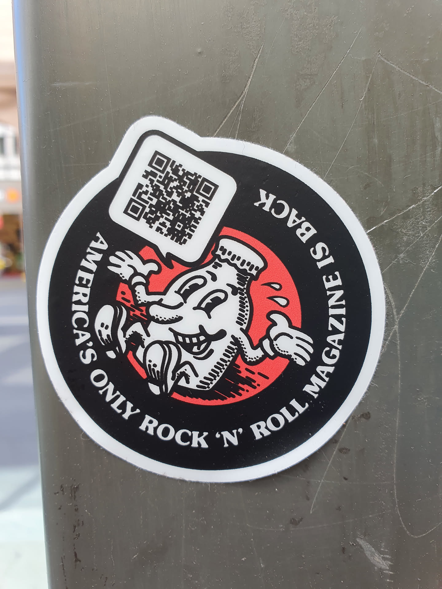 Round sticker featuring a cartoon illustration of a bottle character with the text 'America's Only Rock 'n' Roll Magazine is Back'. It also includes a QR code.