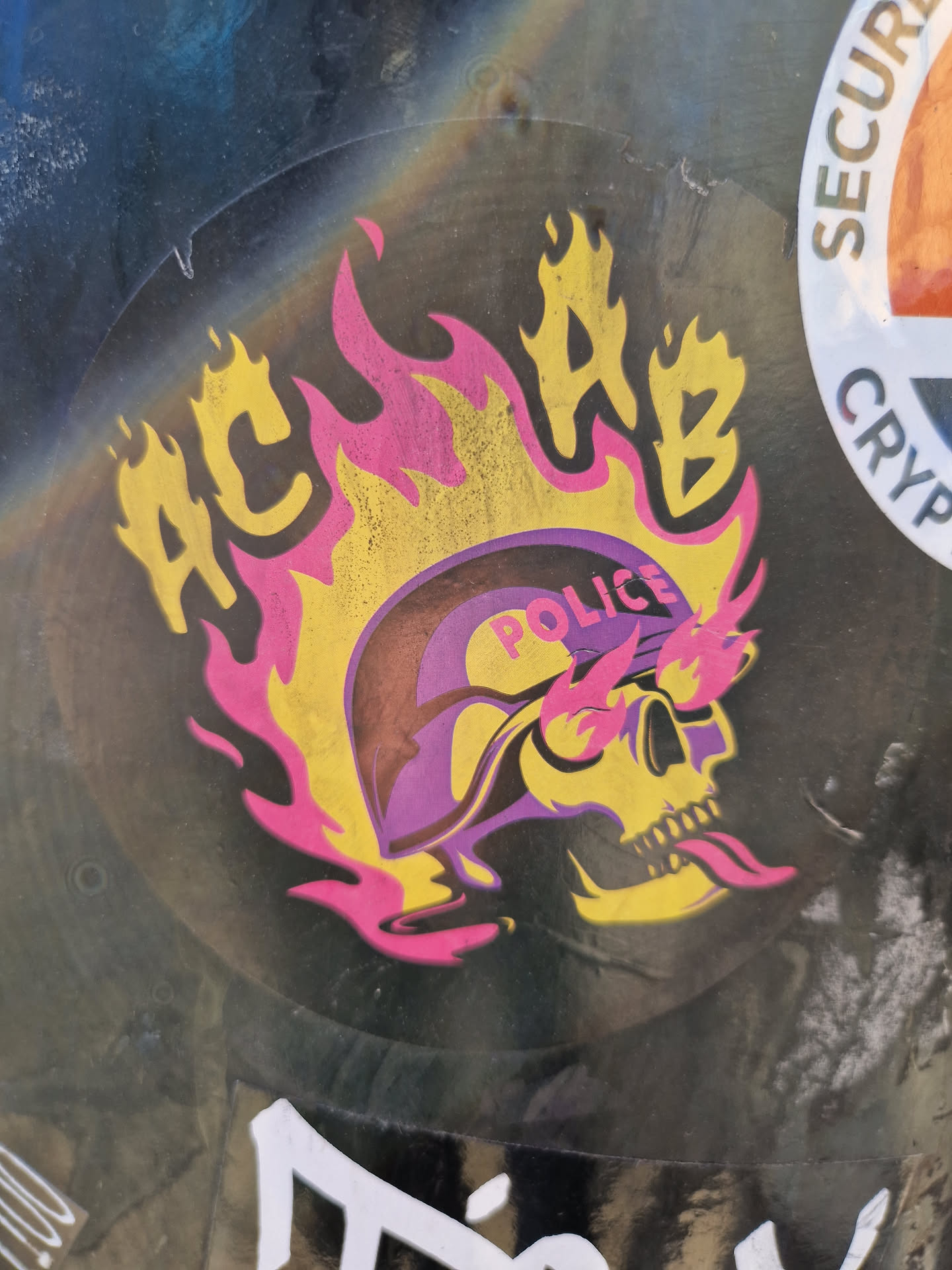A sticker depicting a skull wearing a police helmet engulfed in flames. The acronym ACAB is prominently displayed above the skull. The sticker has a punk aesthetic.