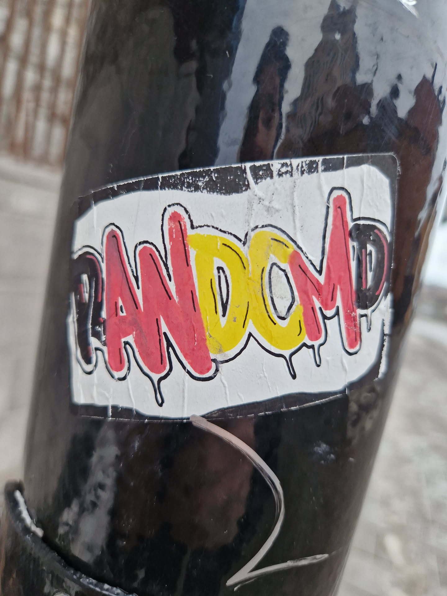 A sticker with the word "RANDOM" written in graffiti-style lettering. The letters are in red, yellow, and black with dripping paint effects. The sticker is slightly worn and peeling at the edges.