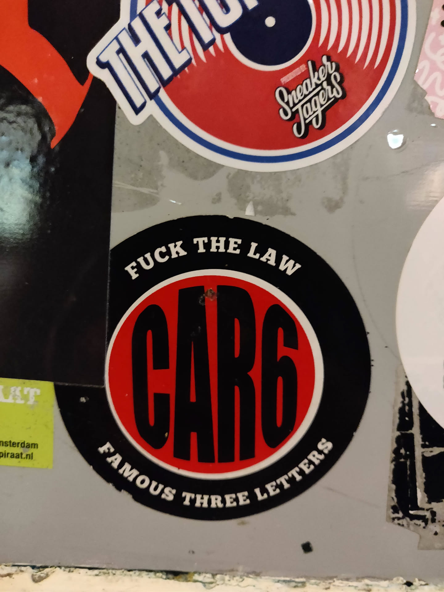 Round sticker with black and red colors. It says CAR6 in big black letters on a red circle. Around the circle it says in smaller letters "FUCK THE LAW" and "FAMOUS THREE LETTERS".