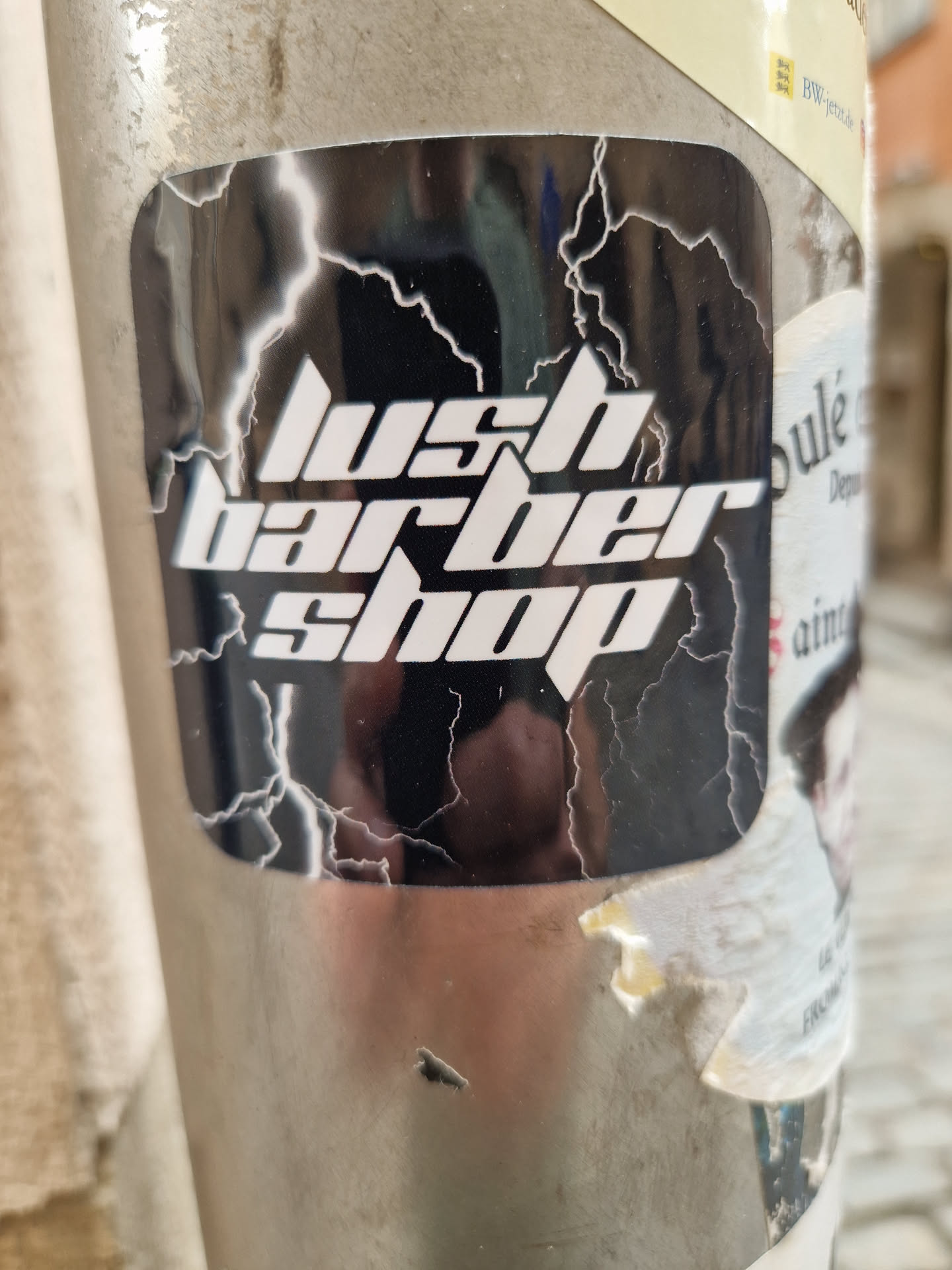 A sticker with the text 'lush barber shop' in white bold letters on a black background with white lightning bolts. The sticker is slightly damaged.
