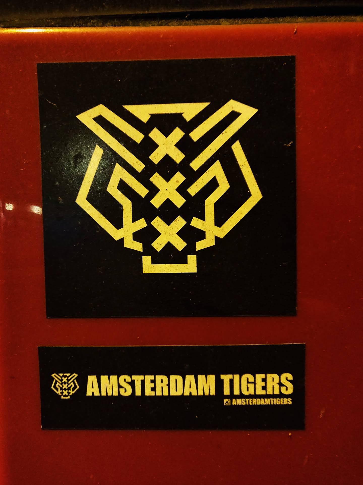 A black and gold sticker featuring a stylized tiger head graphic and the text 'AMSTERDAM TIGERS'.  The lower sticker contains Instagram handle.