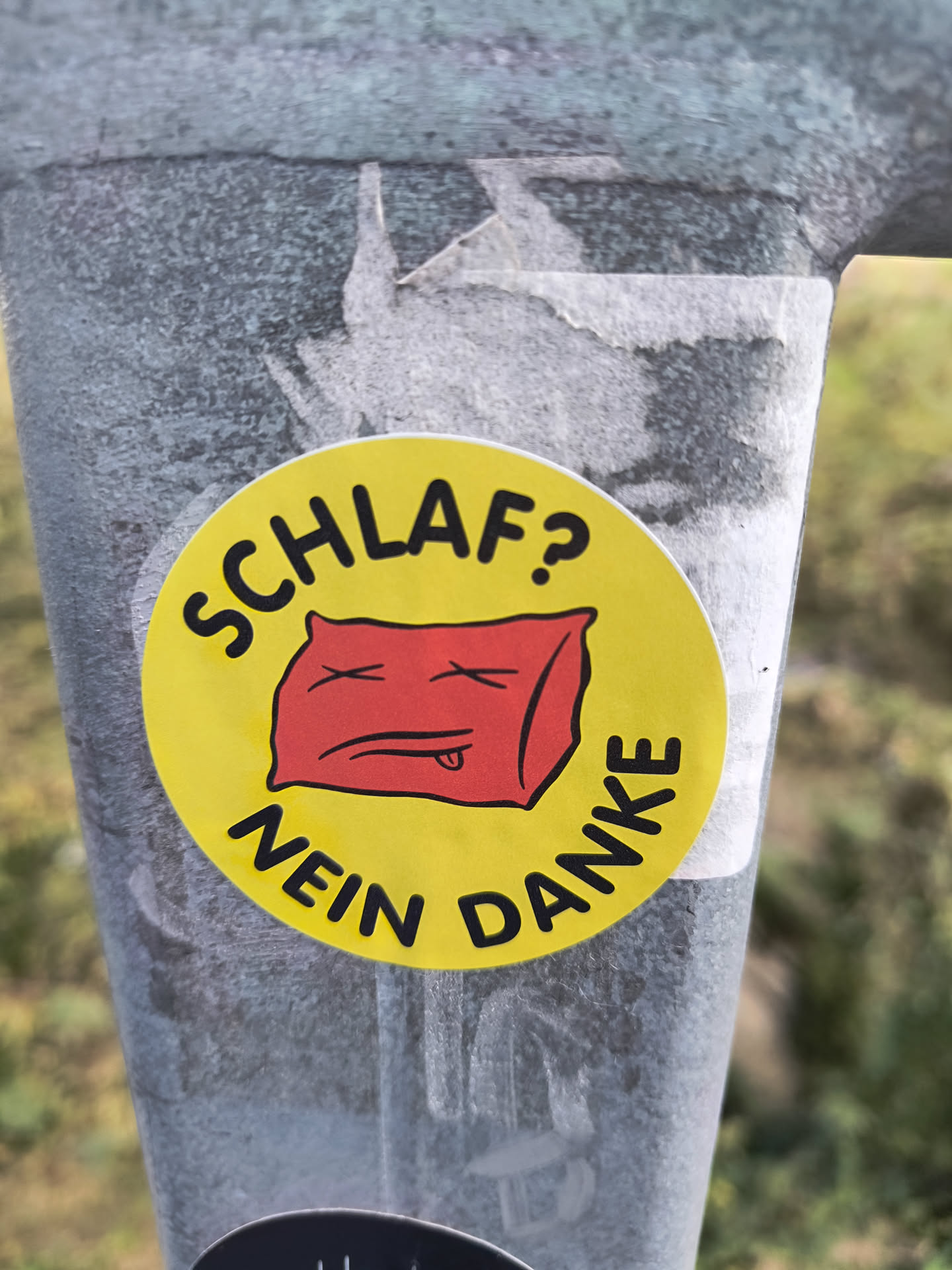 A round yellow sticker with a red cartoon pillow with x eyes and a tongue. The text around it says "Schlaf? Nein Danke" which translates from German to "Sleep? No thanks!"