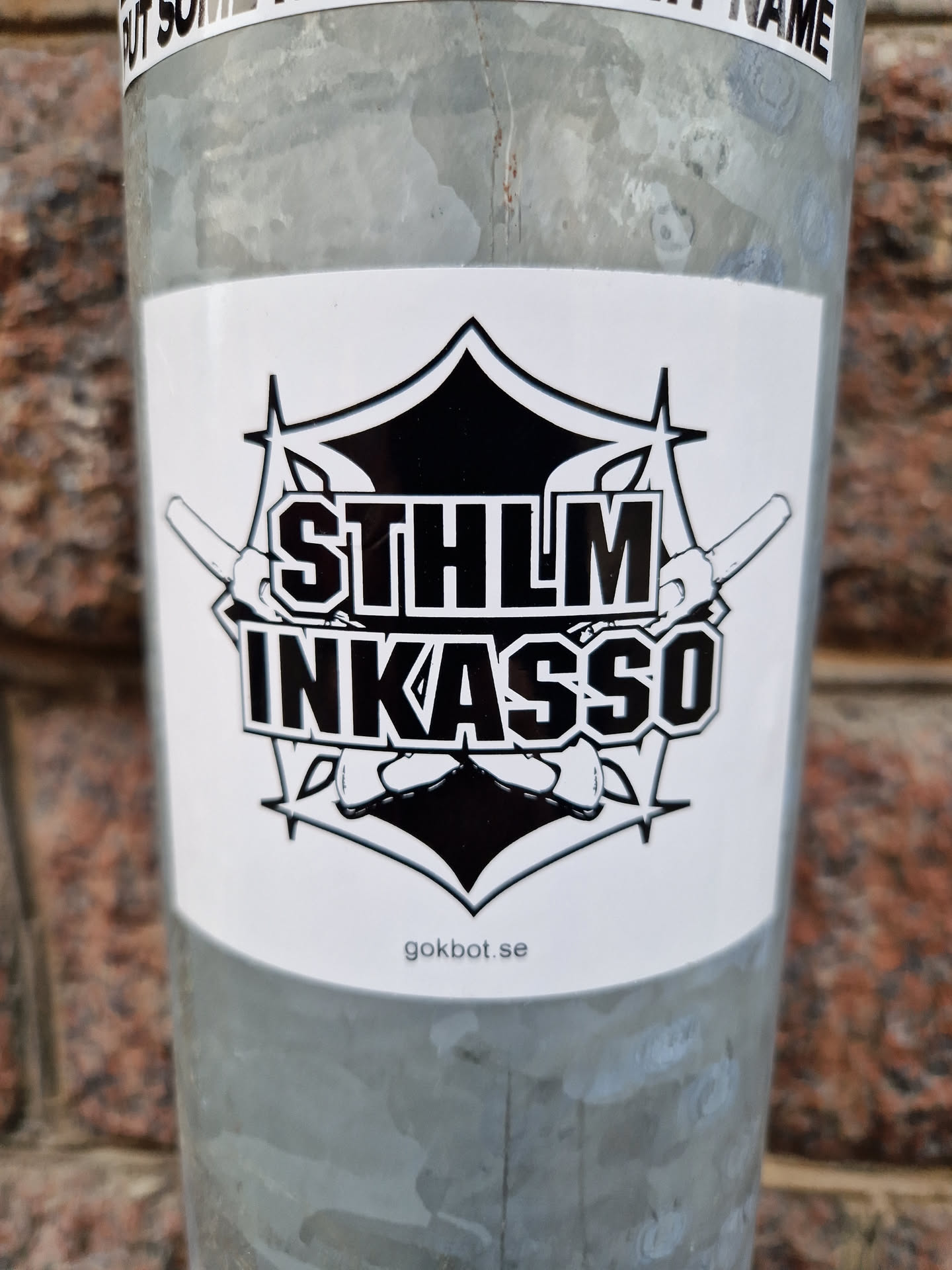 Black and white sticker with a logo featuring the text STHLM INKASSO, crossed swords and a geometric design.  The website gokbot.se is printed at the bottom.